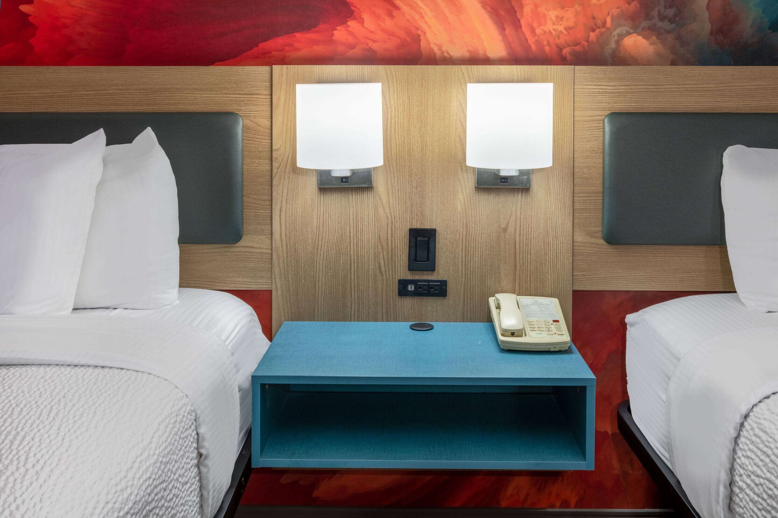 A hotel room with two beds, a blue nightstand, a telephone, and a wall-mounted light fixture.