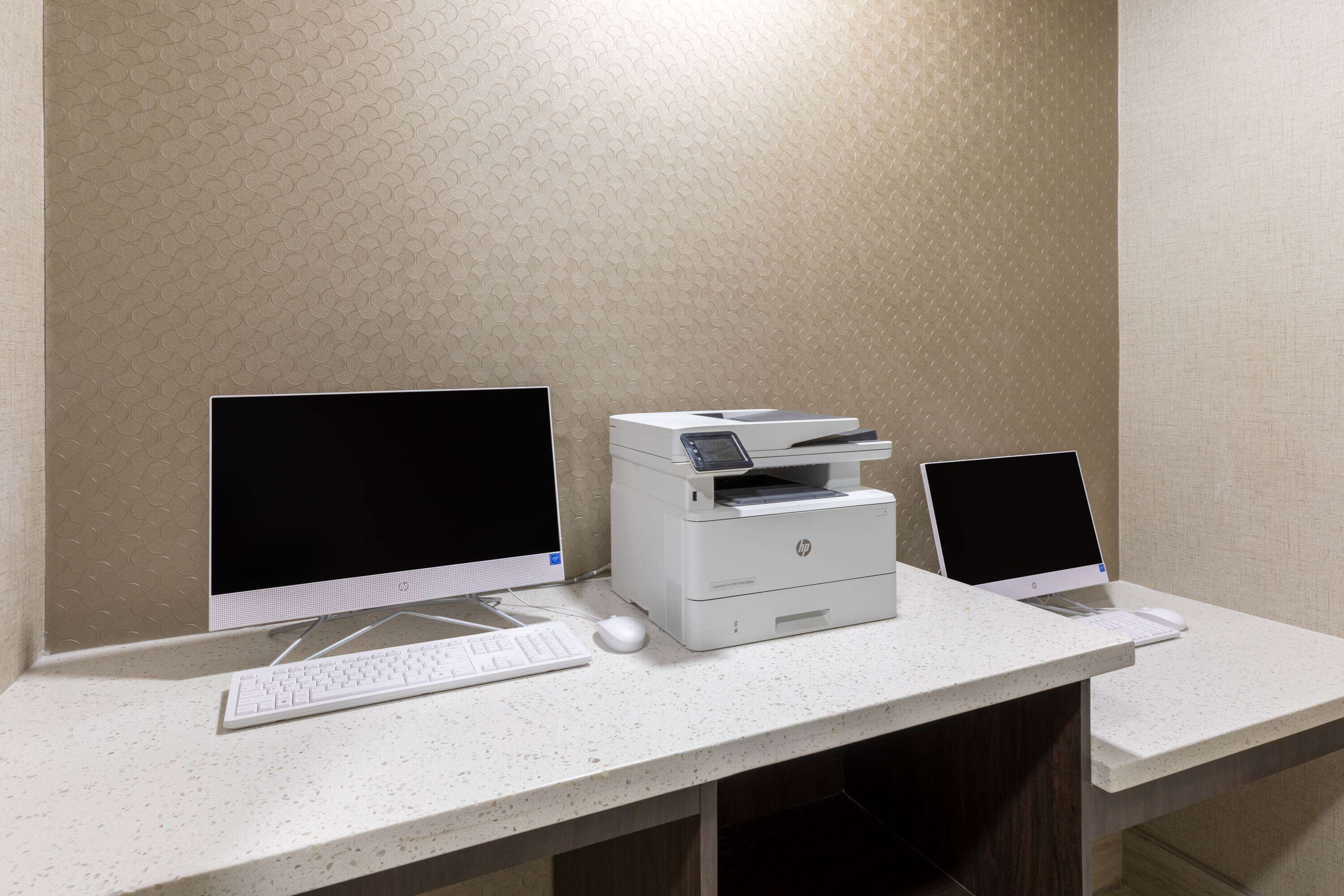A workspace with two desktop computers, a printer, and a keyboard on a white countertop.