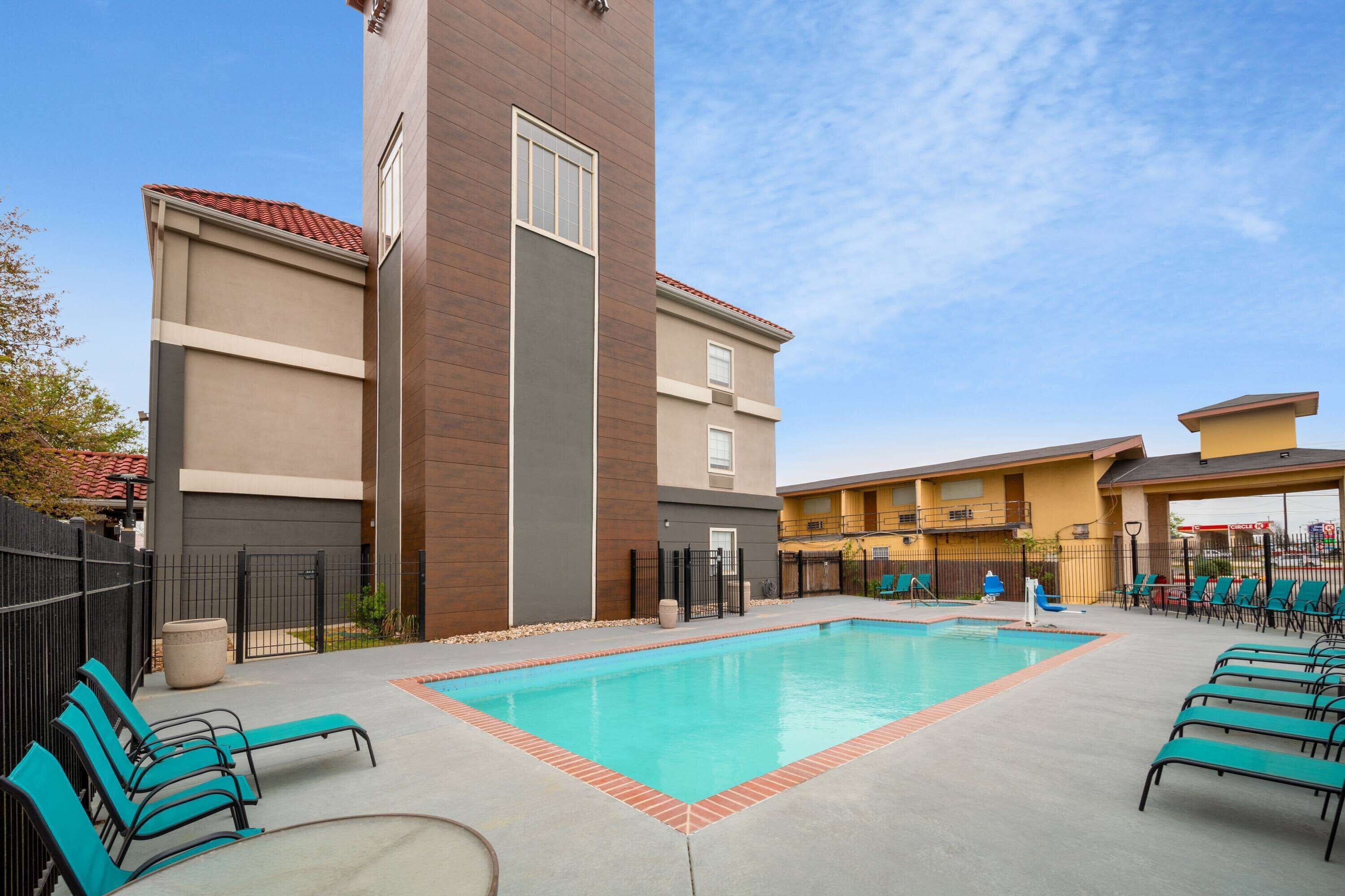 A swimming pool with lounge chairs, a tall building with a red roof, and a clear blue sky.