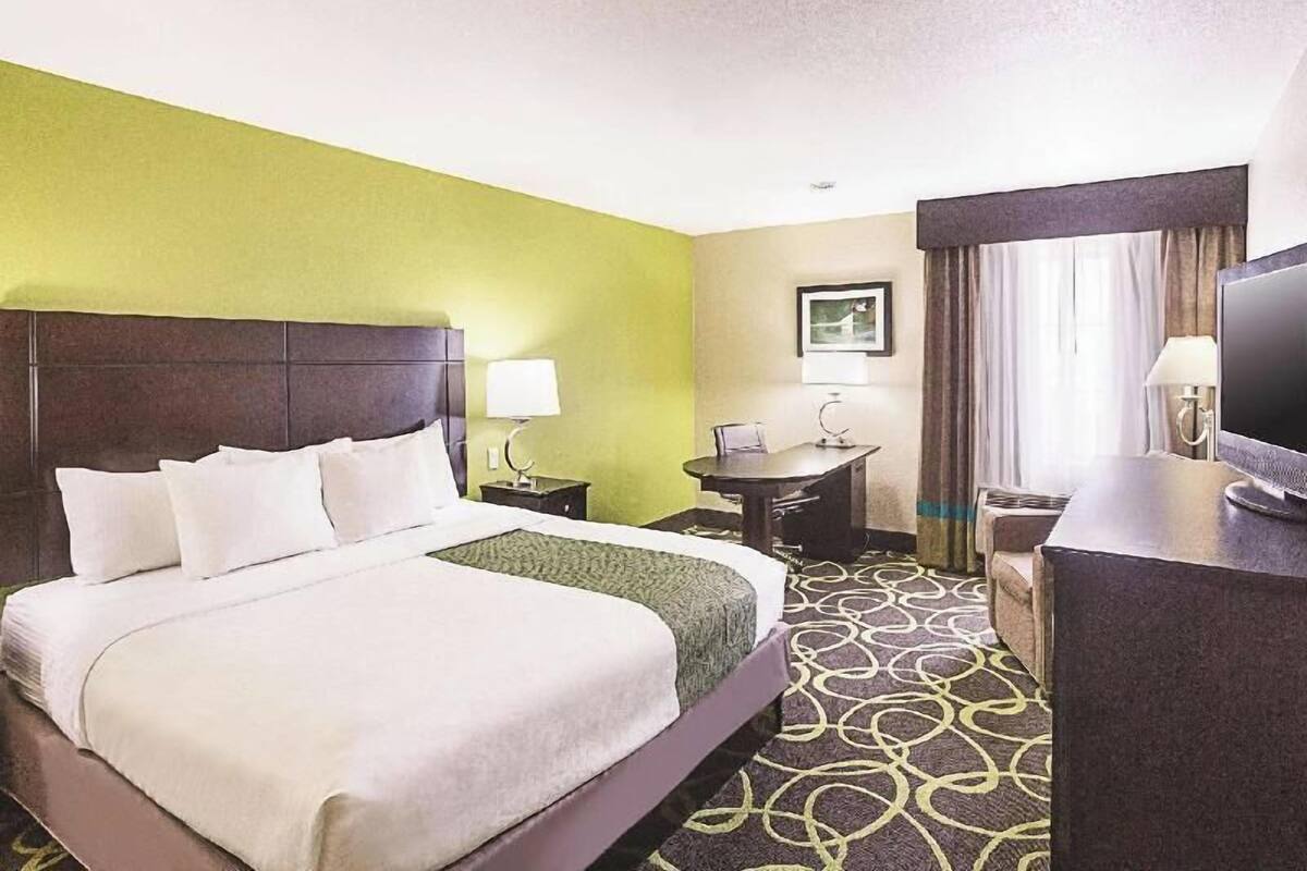 A hotel room with a bed, a desk, a chair, a television, and a window with curtains.