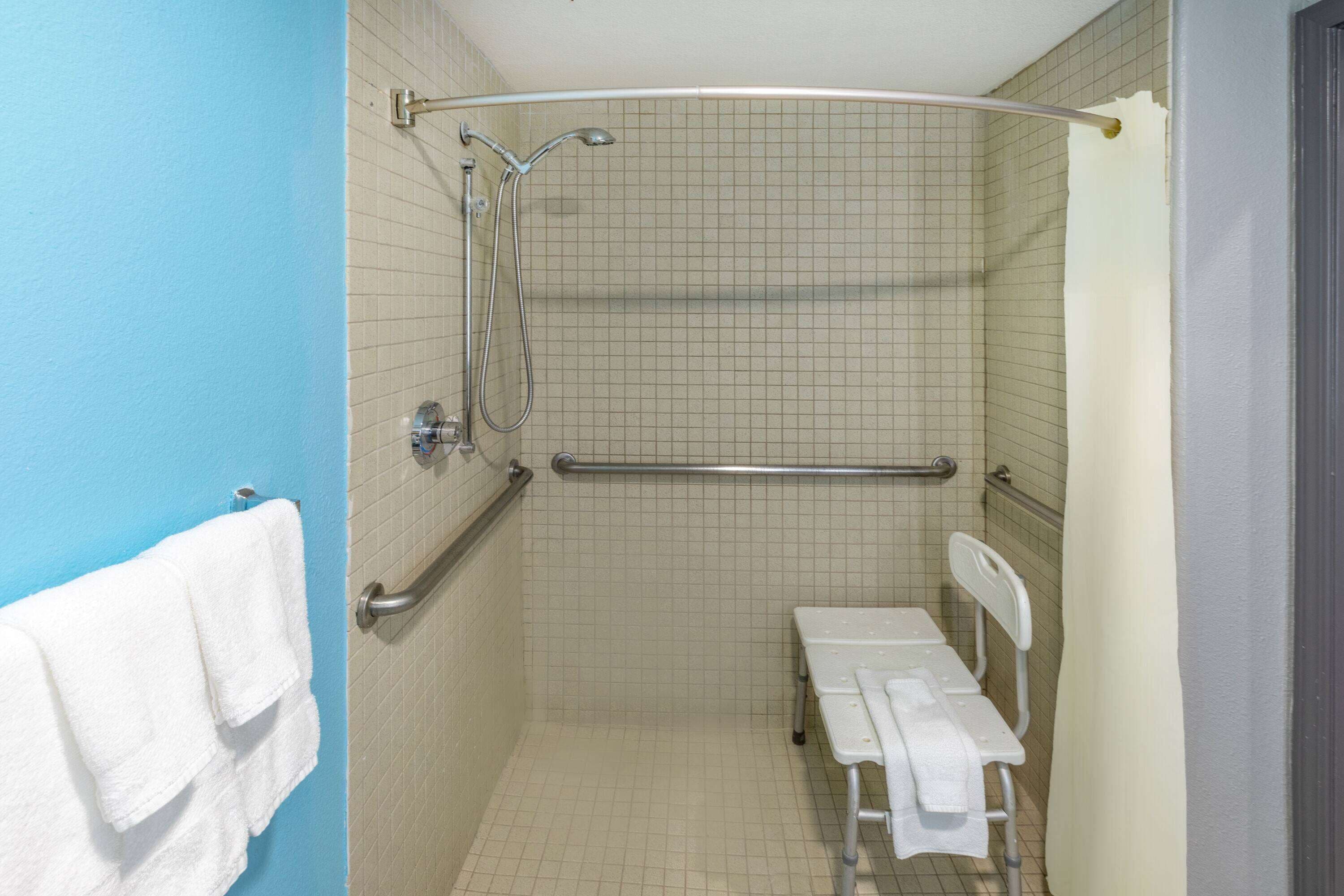 Une salle de bain équipée d’une douche, de barres d’appui, d’un banc et d’un porte-serviettes.