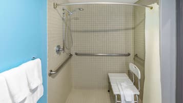 Une salle de bain équipée d’une douche, de barres d’appui, d’un banc et d’un porte-serviettes.