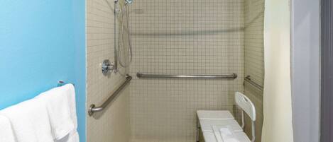 A bathroom with a shower, grab bars, a bench, and a towel rack.