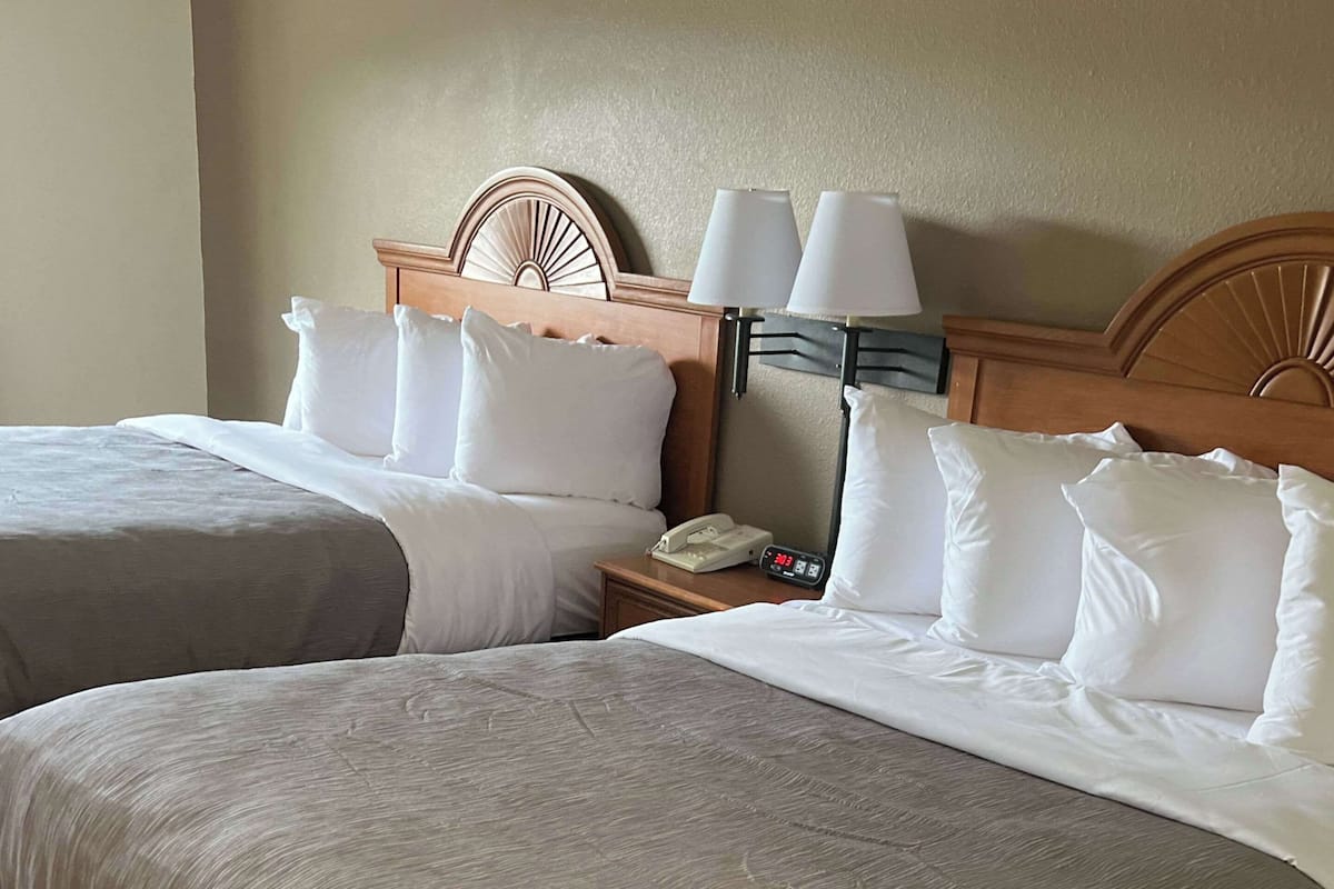 Ein Hotelzimmer mit zwei Betten, jeweils mit weißer Bettwäsche und Kissen, einem hölzernen Kopfteil, einem Nachttisch mit Lampe und einem Telefon.