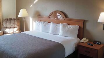A hotel room with a large bed, a wooden headboard, a bedside table with a phone and remote control, and a chair.