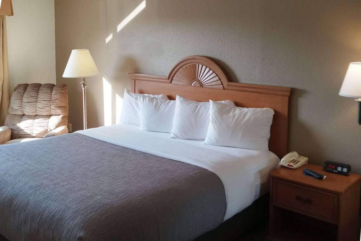 Ein Hotelzimmer mit einem Bett, einem Nachttisch mit Telefon und Fernbedienung, einem Sessel und einer Lampe.