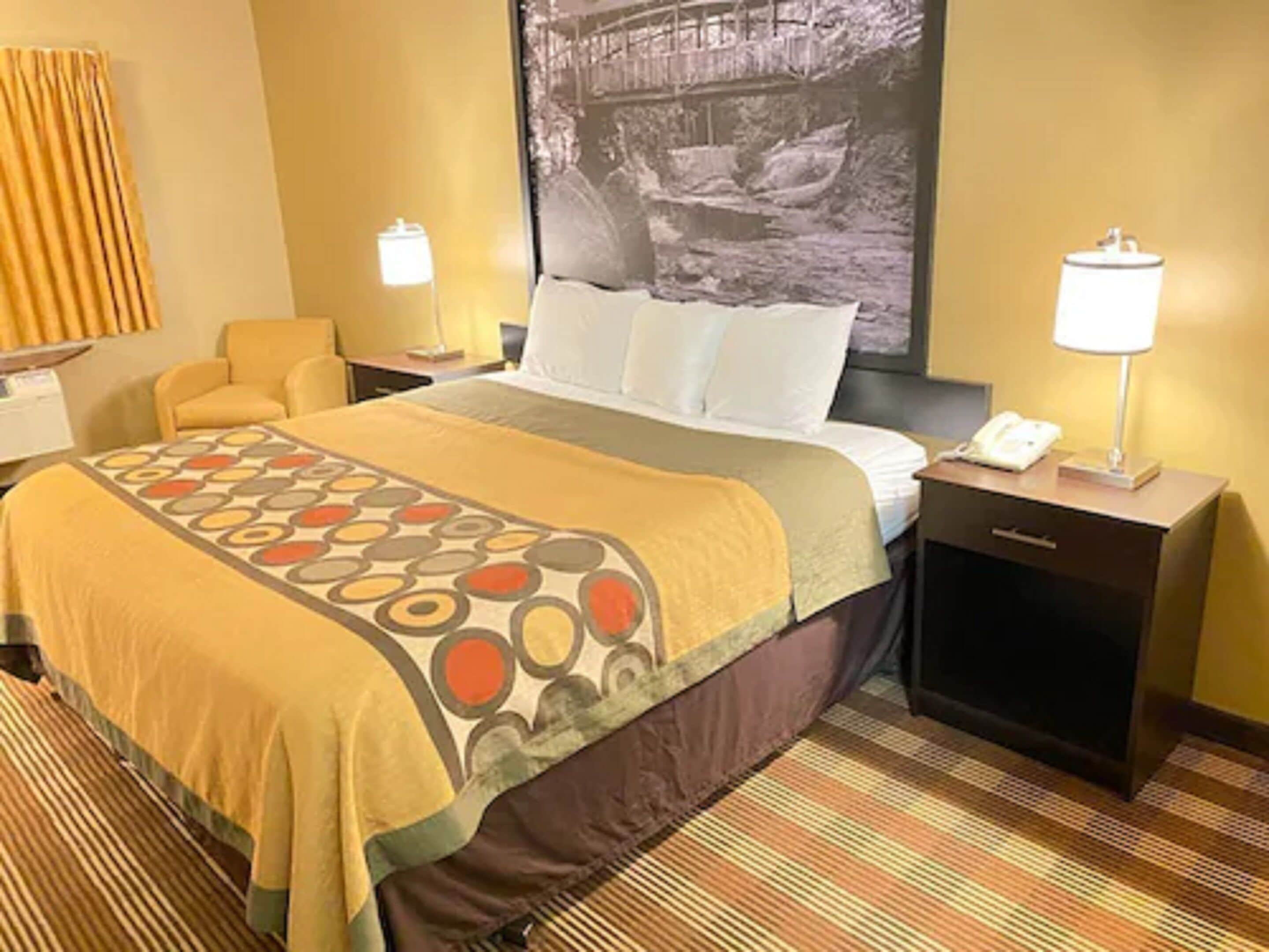 Une chambre d’hôtel avec un lit, des tables de chevet, une lampe et un grand tableau encadré au mur.