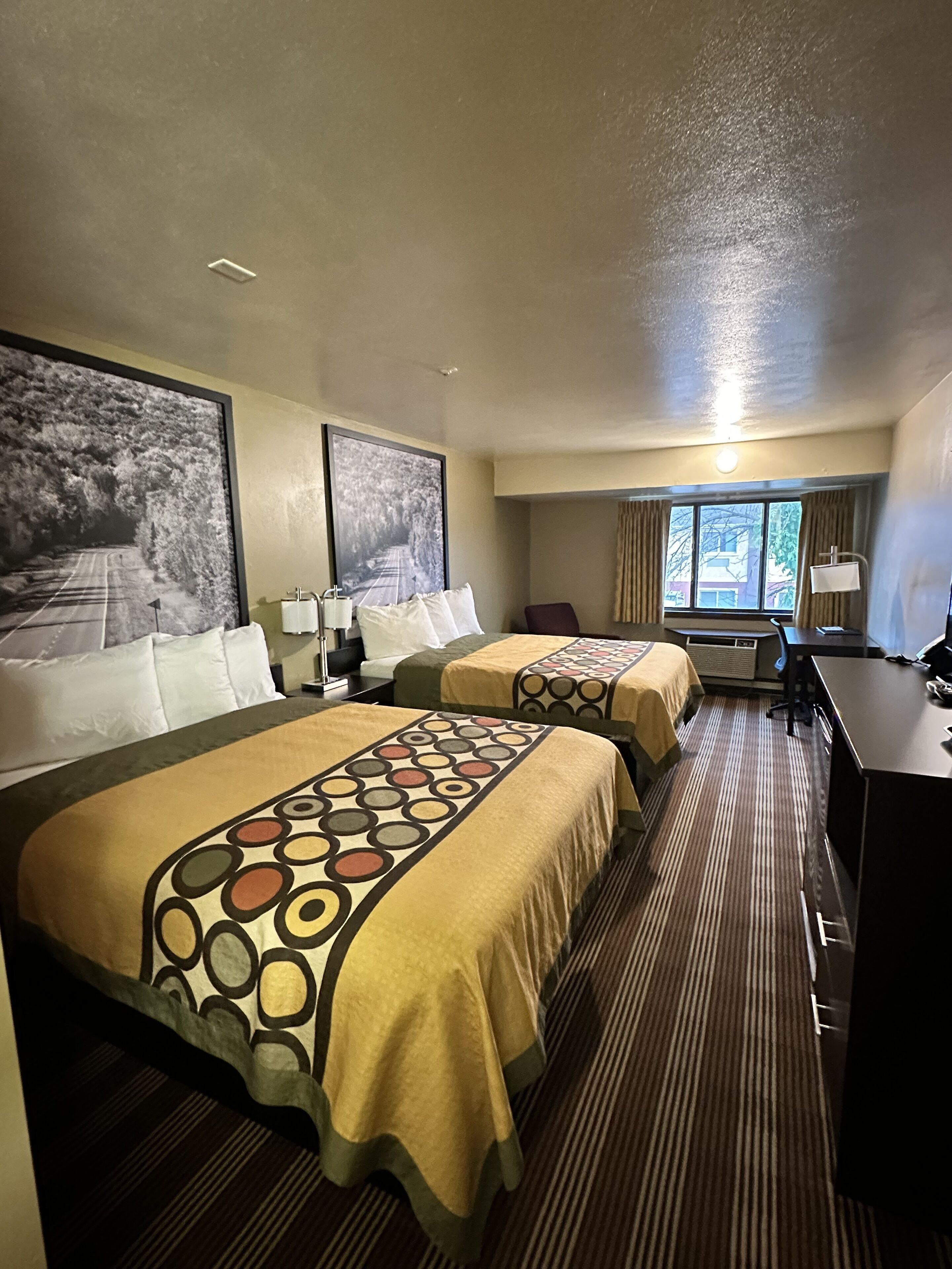 Une chambre d’hôtel avec deux lits, un bureau, une chaise et une grande fenêtre.