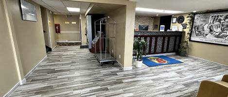 A hotel lobby with a herringbone-patterned floor, a reception desk, a fire extinguisher, and a large framed poster on the wall.