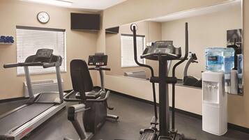 A gym with treadmills, an elliptical, and a stationary bike. There is a water dispenser and a clock on the wall.