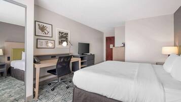 A hotel room with a bed, desk, chair, TV, and artwork on the wall.
