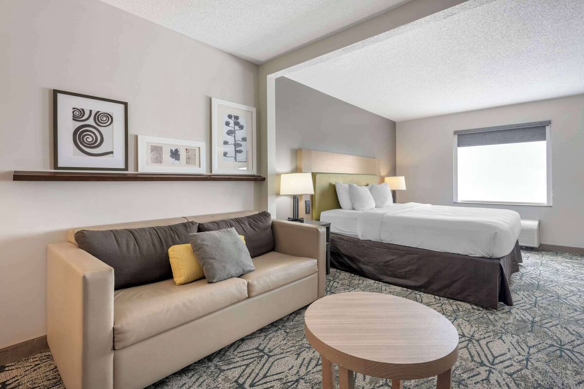 A hotel room with a sofa, a round table, a bed, and artwork on the wall.