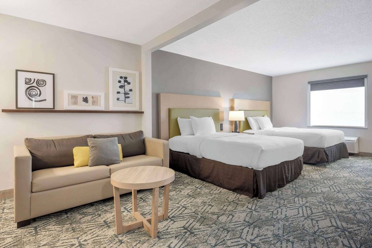 A hotel room with a sofa, two single beds, a small table, and artwork on the wall.
