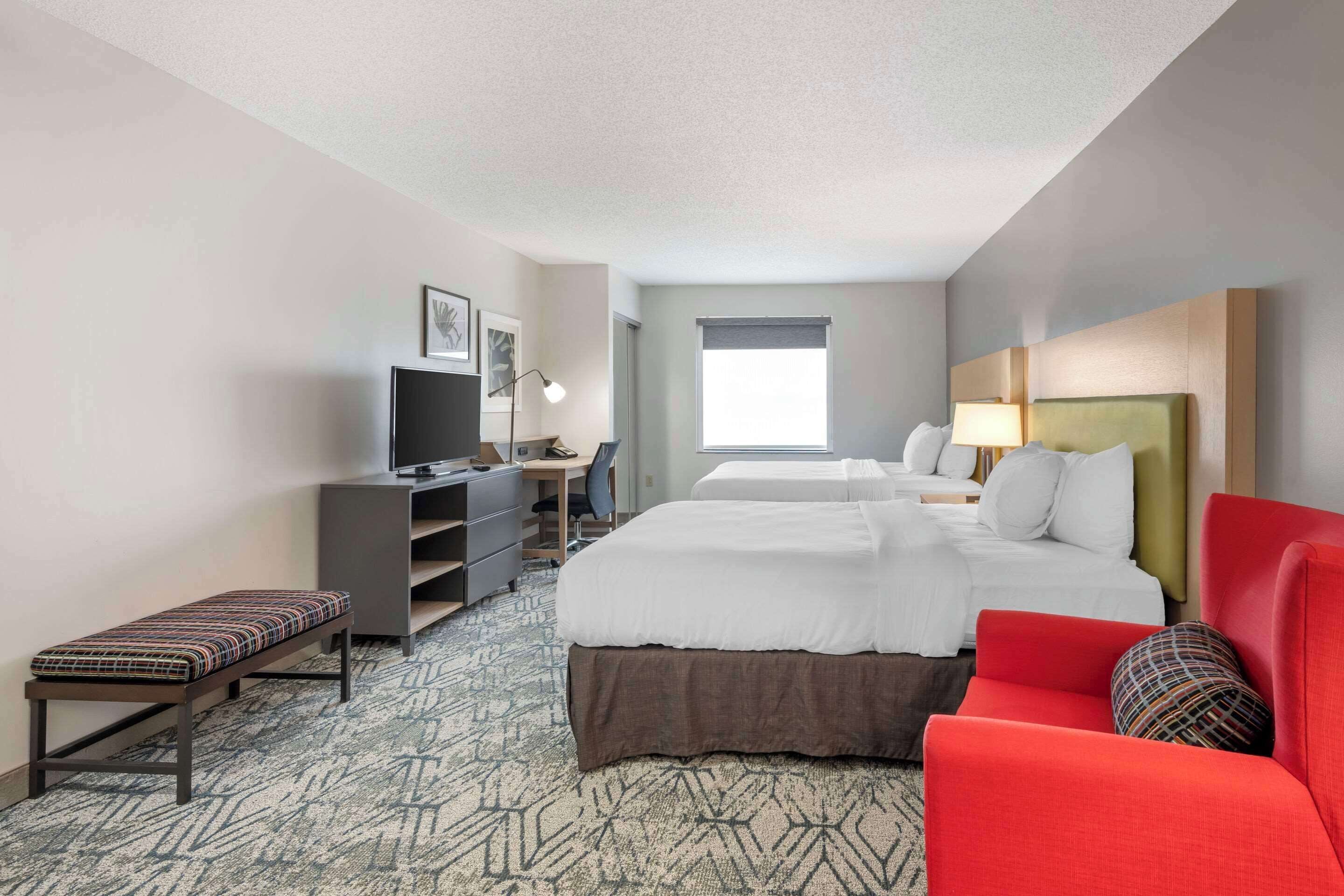 A hotel room with a large bed, a desk with a computer, a chair, and a bench.