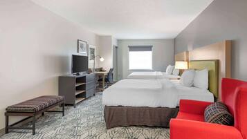 A hotel room with a large bed, a desk with a computer, a chair, and a bench.