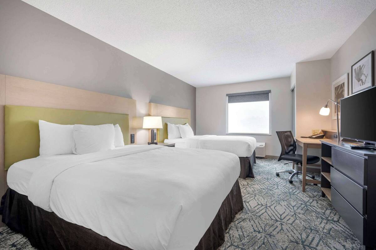 A hotel room with two beds, a desk, a chair, a TV, and a window.