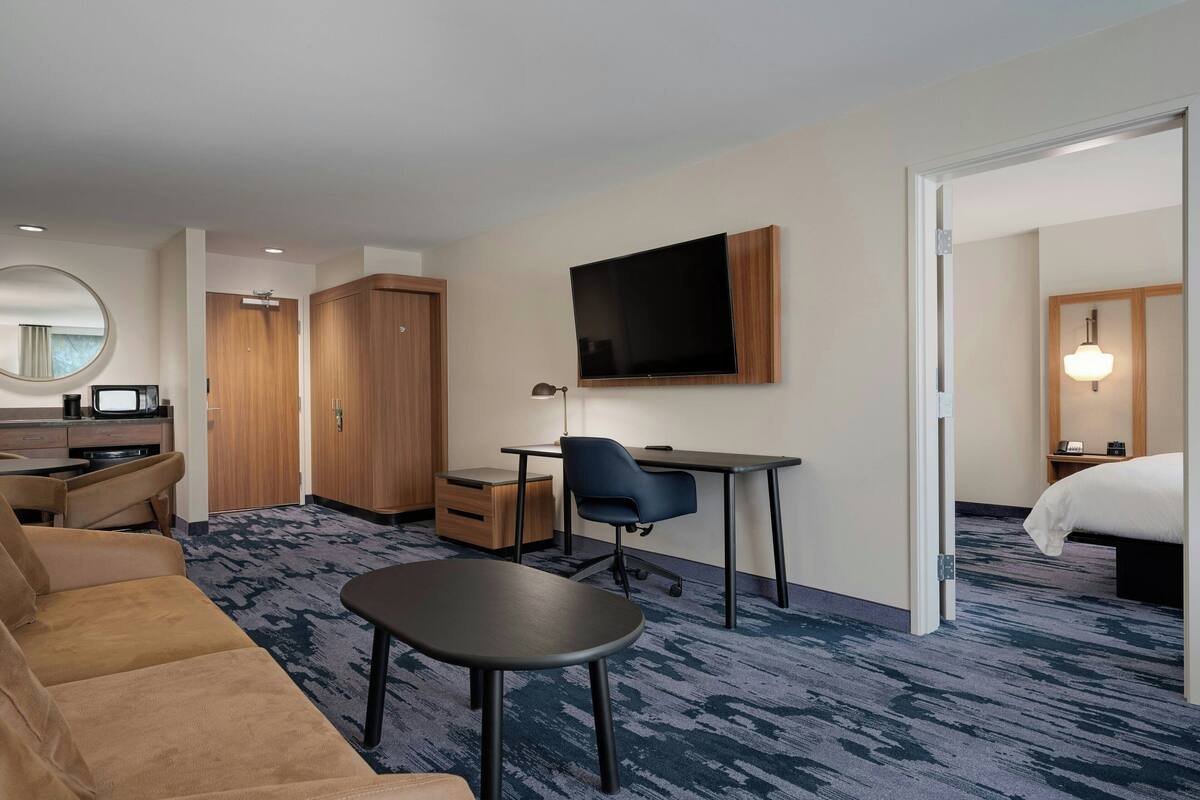 A hotel room with a sofa, a desk, a chair, a TV, a wardrobe, and a bed.