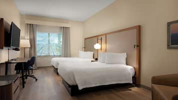 Habitación de hotel con dos camas, un escritorio con silla, televisor, lámpara y ventana con cortinas.