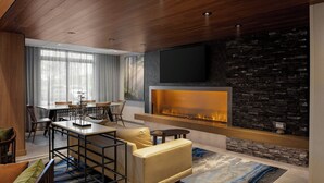 A modern living room with a fireplace, a dining area, and a TV mounted on a stone wall. - Fairfield by Marriott Inn & Suites Missoula Airport (Missoula)