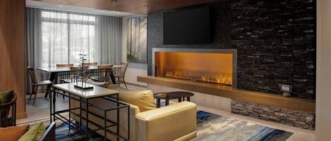 A modern living room with a fireplace, a dining area, and a TV mounted on a stone wall.