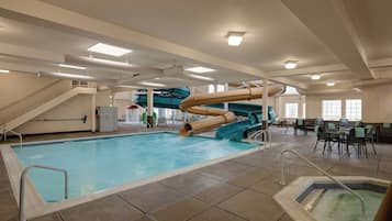 Une piscine intérieure avec un toboggan, un jacuzzi et un escalier menant à un niveau supérieur.