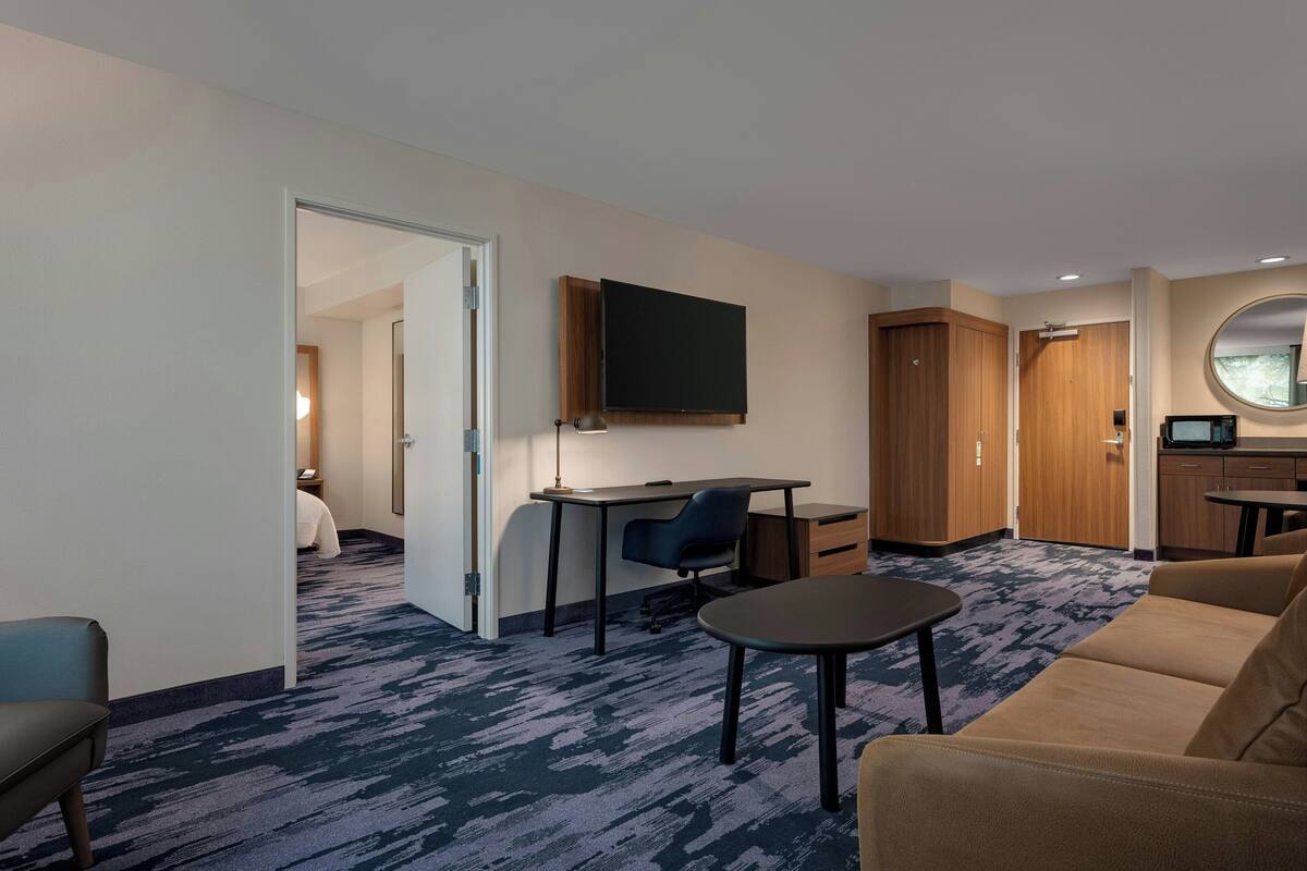 A hotel room with a desk, chair, sofa, and a TV mounted on the wall.