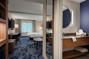 A hotel room with a bed, desk, chair, round table, and a bathroom with a sink and mirror. - Fairfield by Marriott Inn & Suites Missoula Airport (Missoula)