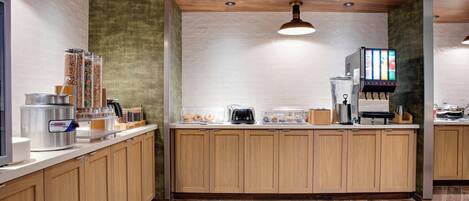 Una cocina moderna con armarios de madera, una máquina de café, un dispensador de alimentos y un menú digital.