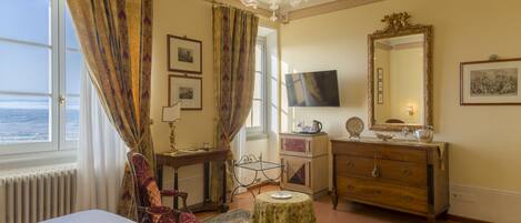 Habitación de hotel con cama, escritorio, silla, cómoda, televisor y ventana grande con cortinas.