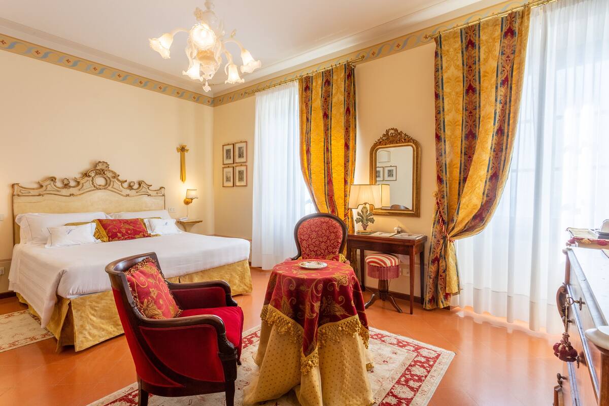 A hotel room with a large bed, a desk, a chair, and a table with a red tablecloth.