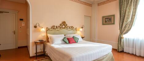 A hotel room with a large bed, a chandelier, a small table, and a door leading to another room.