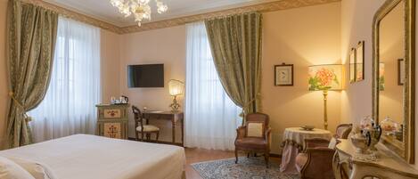 Habitación de hotel con una cama grande, un escritorio con silla, una mesita de noche con lámpara, una silla, un espejo y un tapete decorativo.