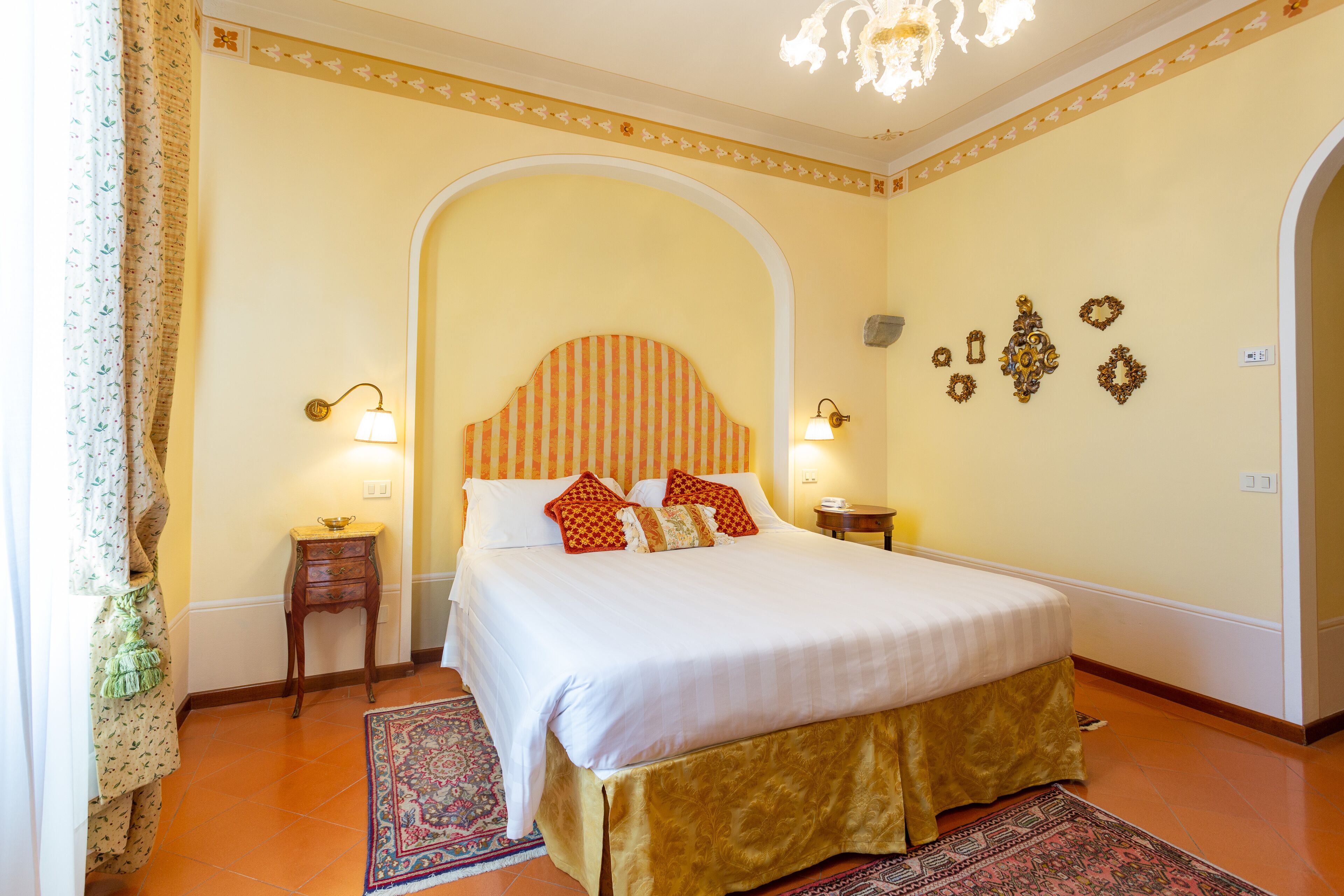 Habitación de hotel con una cama grande, dos mesitas de noche, un candelabro y apliques decorativos.