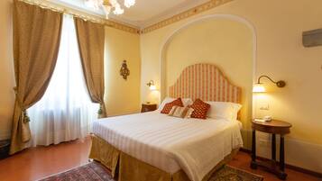 A hotel room with a large bed, two bedside tables, a chandelier, and a view of the outdoors through curtains.
