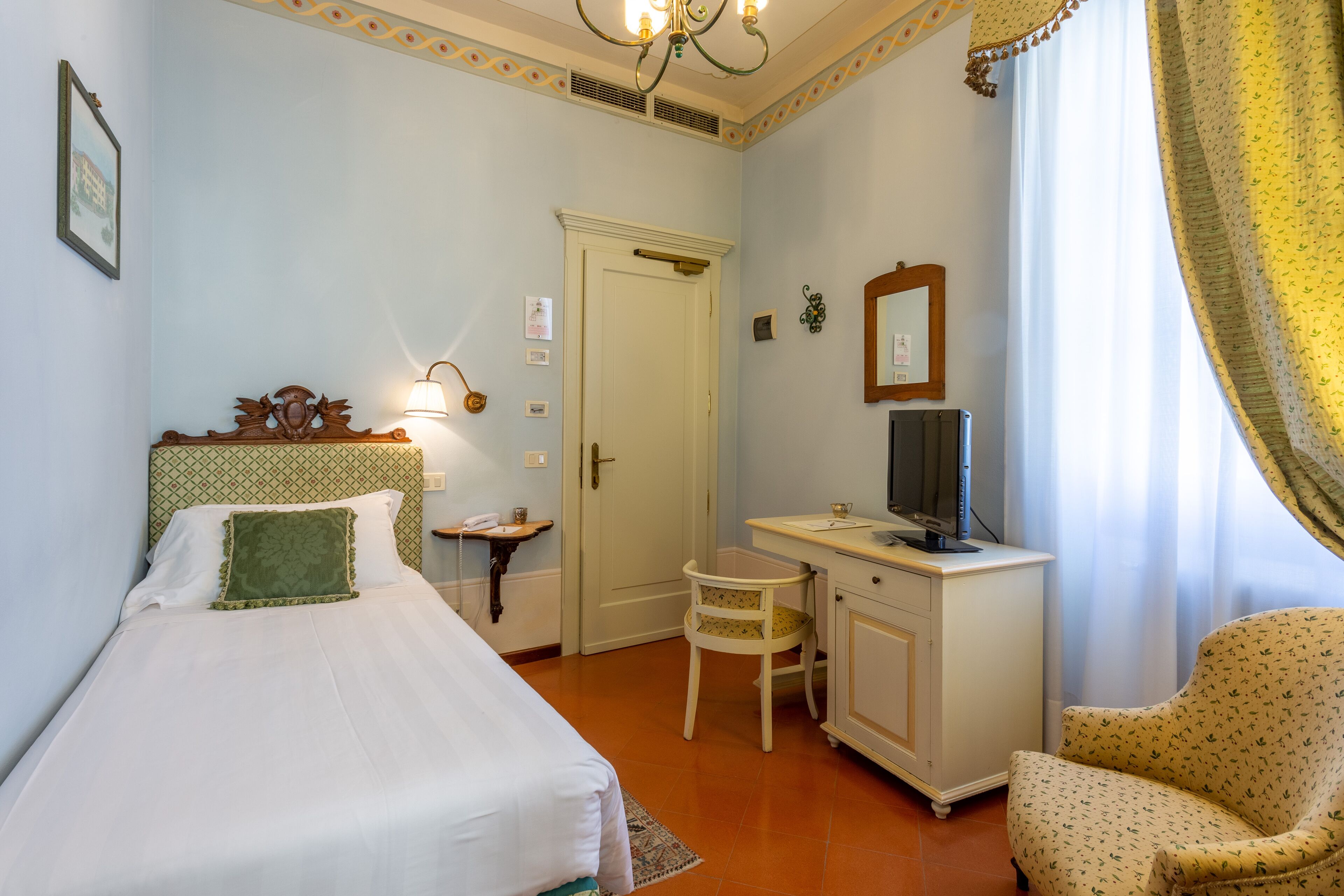 Habitación de hotel con cama, escritorio con ordenador, silla, mesita pequeña y espejo.