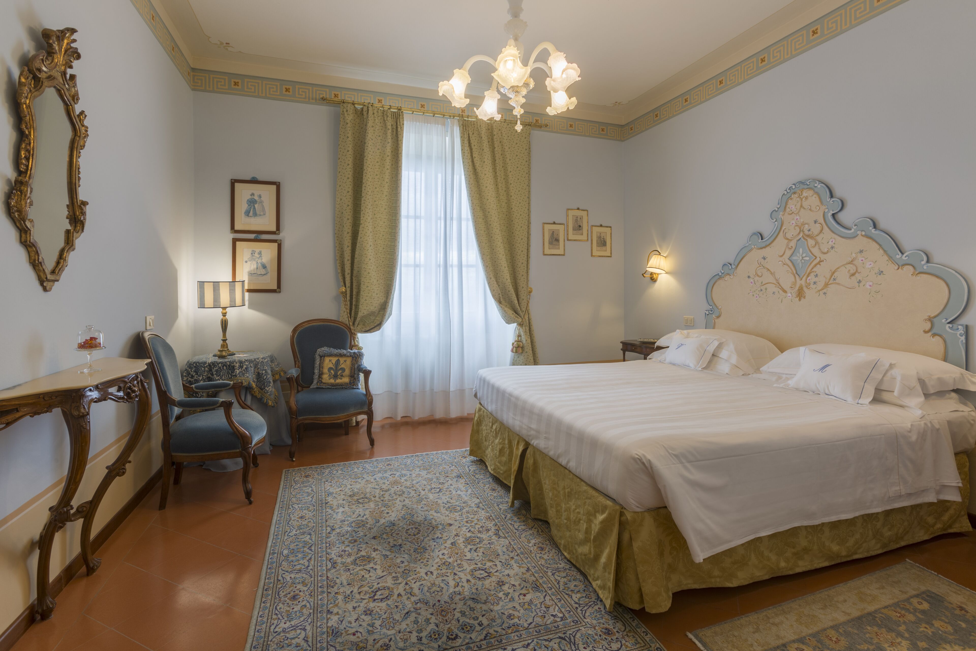 A bedroom with a large bed, a desk, a chair, and a chandelier.