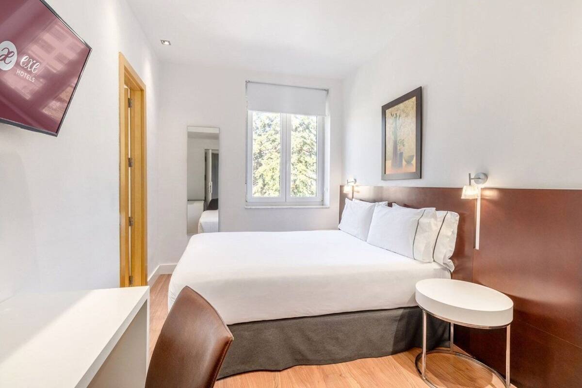 Une chambre d’hôtel avec un lit, une table de chevet, une chaise et une fenêtre donnant sur des arbres.