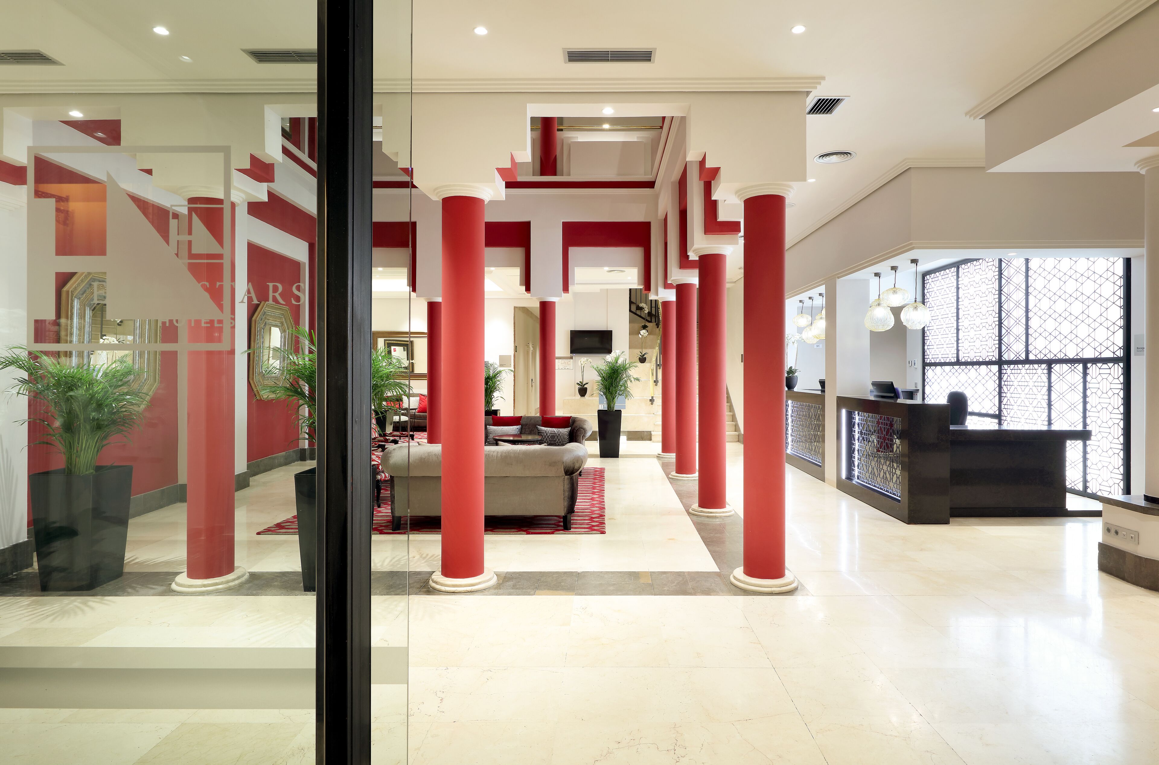 Un vestíbulo espacioso con columnas rojas, un mostrador de recepción y una zona de estar con alfombra roja.