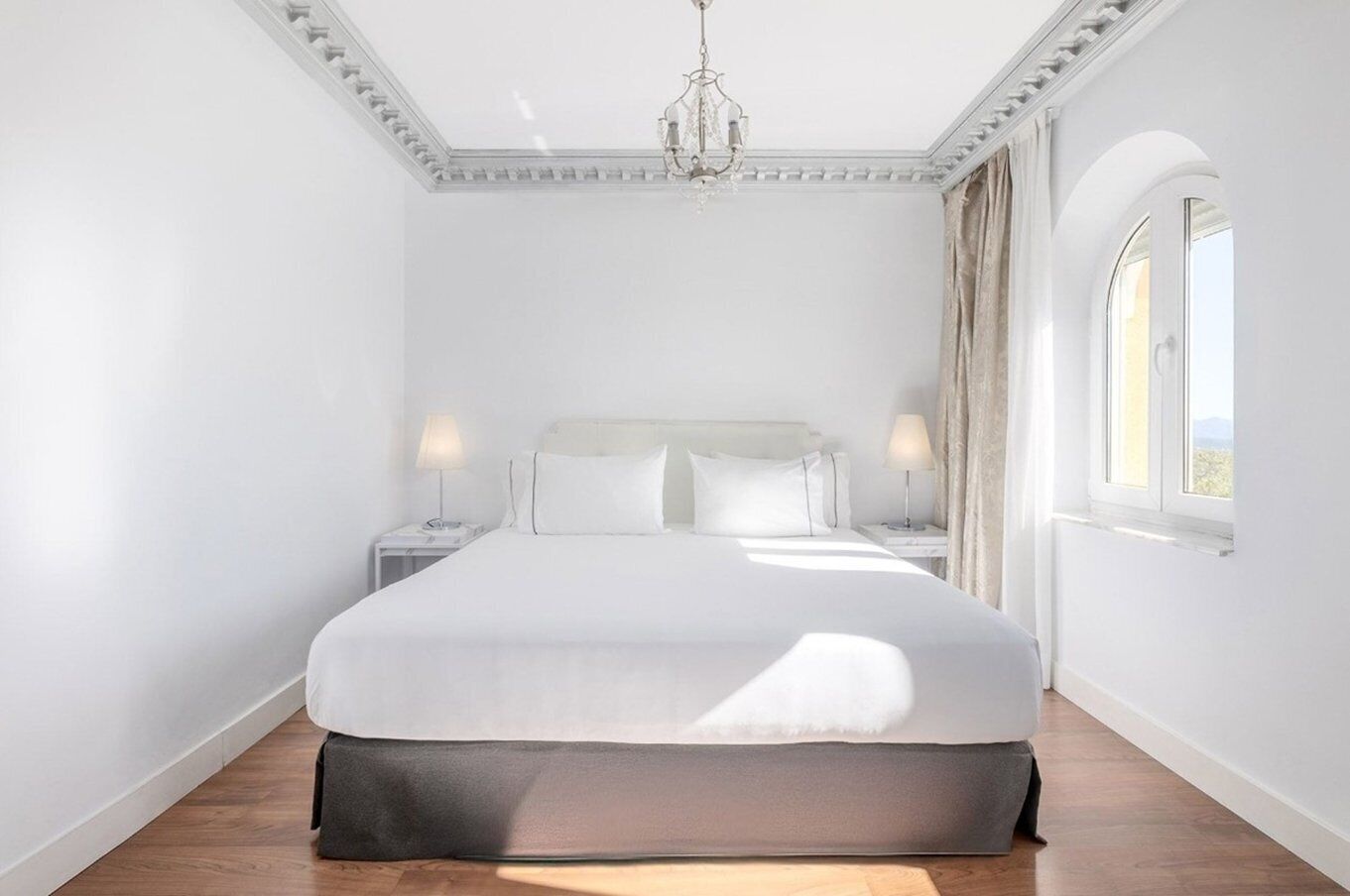 A spacious bedroom with a large bed, a chandelier, and a window with curtains.