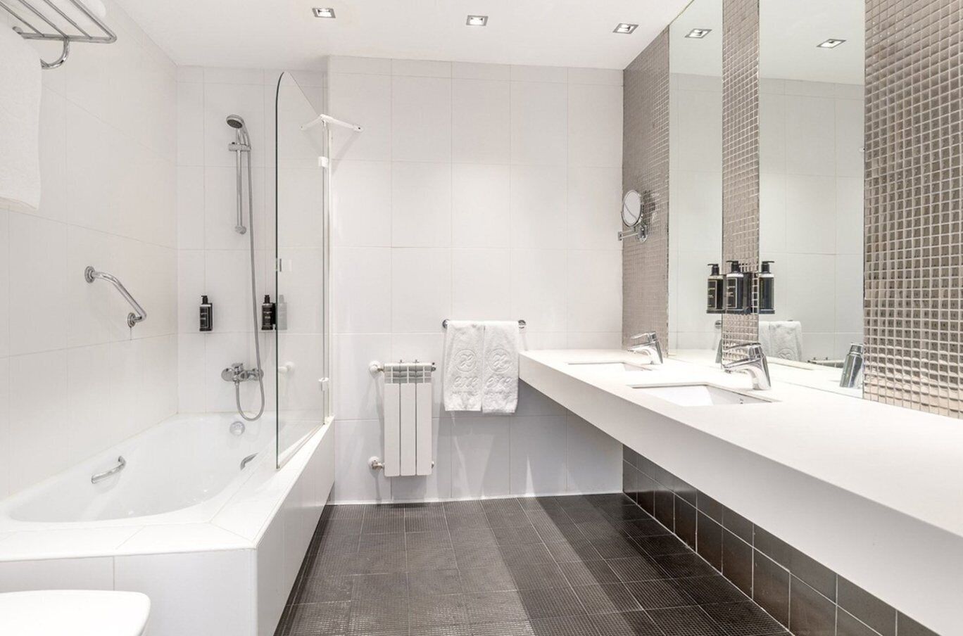 A modern bathroom with a bathtub, shower, and a large mirror.