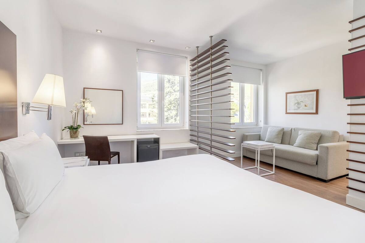 Une chambre d’hôtel moderne équipée d’un grand lit, d’un bureau, d’une chaise, d’un canapé et d’un radiateur.
