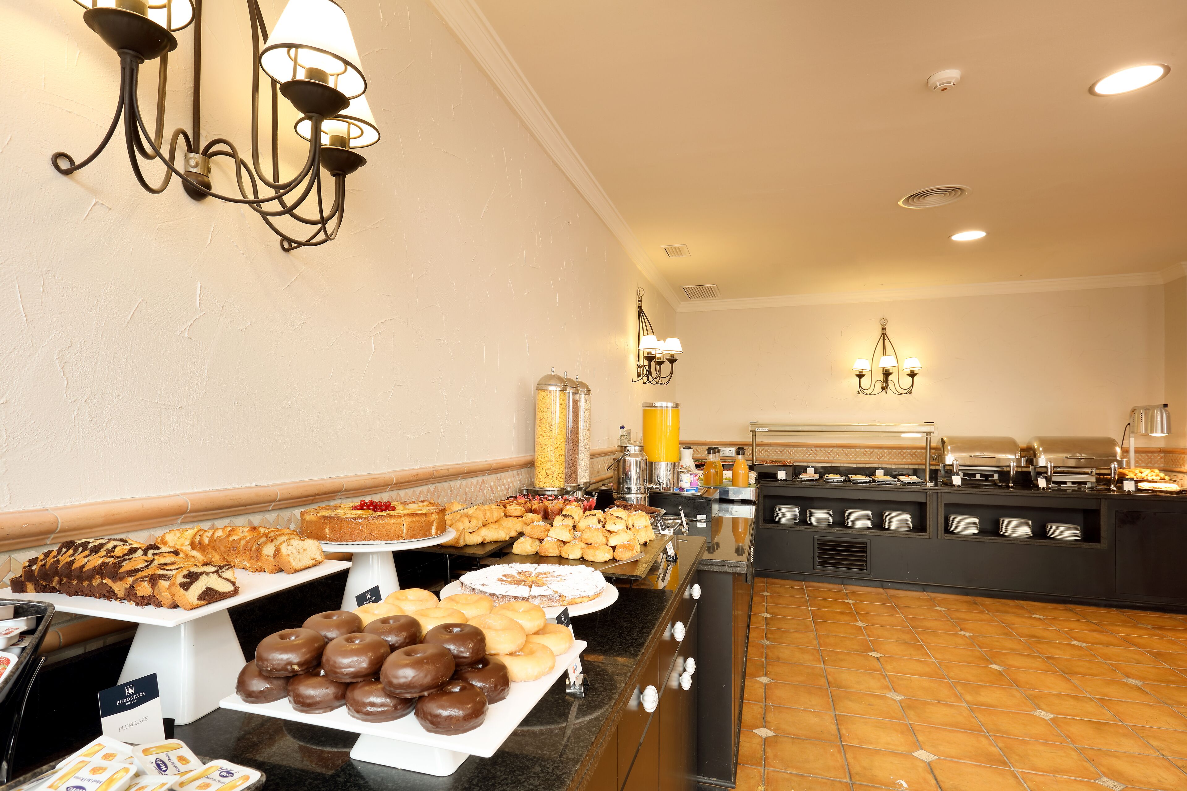 Un bufé con diversos pasteles y postres, una estación de café y una barra de zumos.