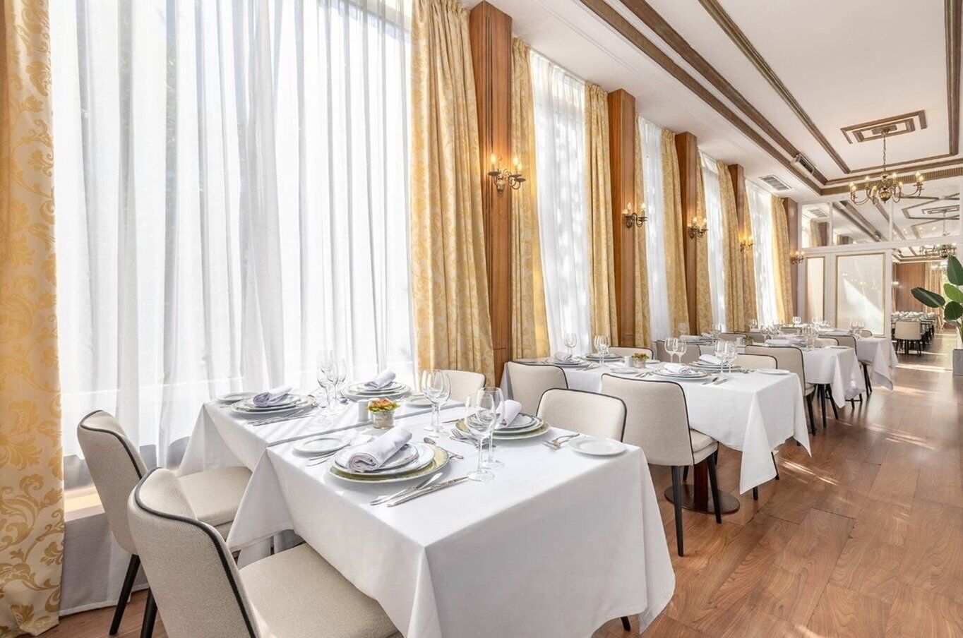 Un restaurante con varias mesas dispuestas para comer, con manteles blancos y detalles dorados.