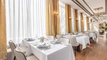 Un restaurante con varias mesas dispuestas para comer, con manteles blancos y detalles dorados.