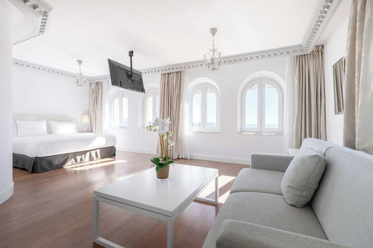 Une chambre d’hôtel moderne équipée d’un lit, d’un canapé, d’une télévision et de grandes fenêtres.
