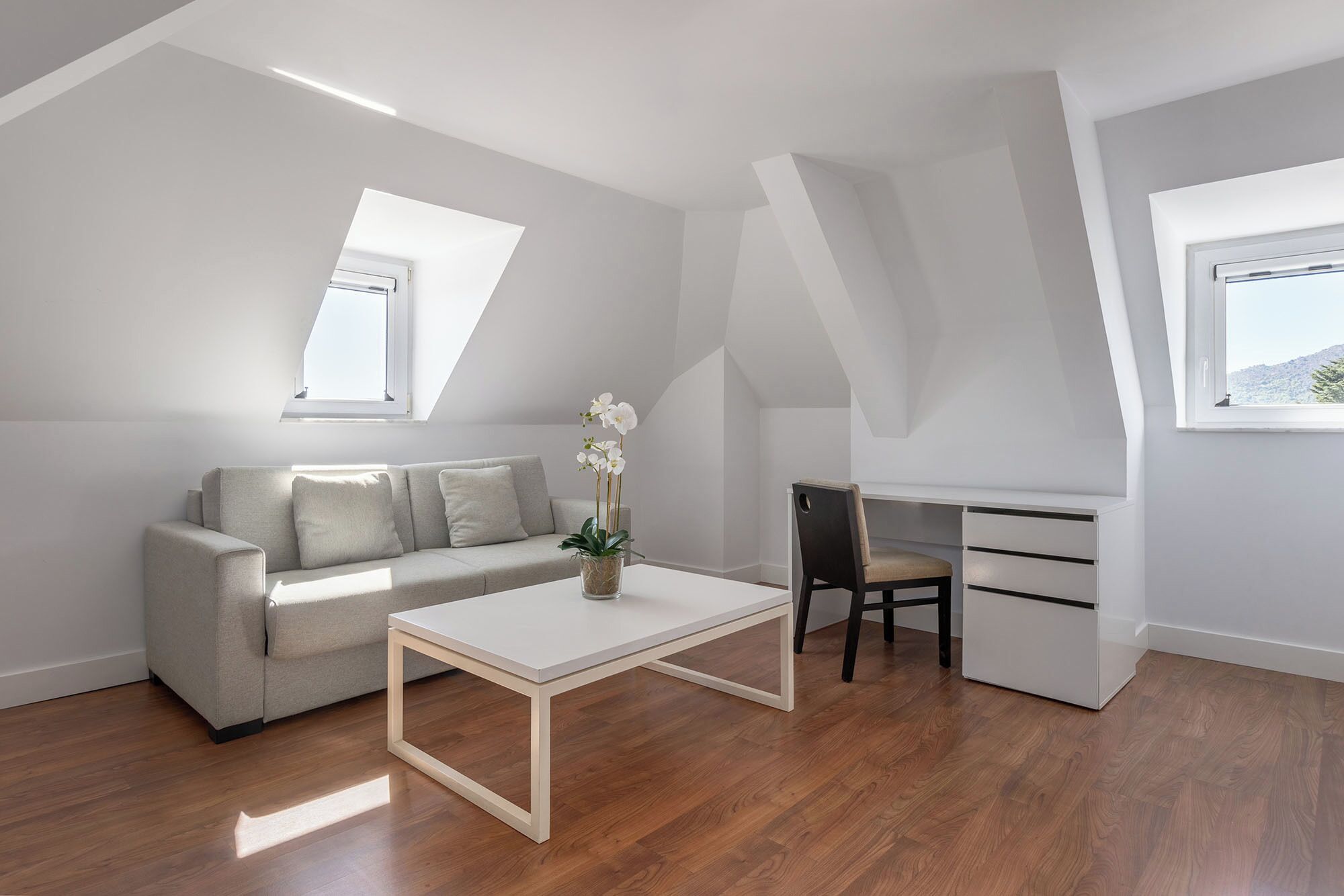 Un dormitorio estilo loft moderno con techo inclinado, un sofá, un escritorio y una mesita de centro.