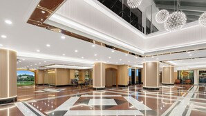 A spacious lobby with a polished marble floor, large columns, and a view of a park through the glass wall. - Riviera Hotel Macau (Macau)