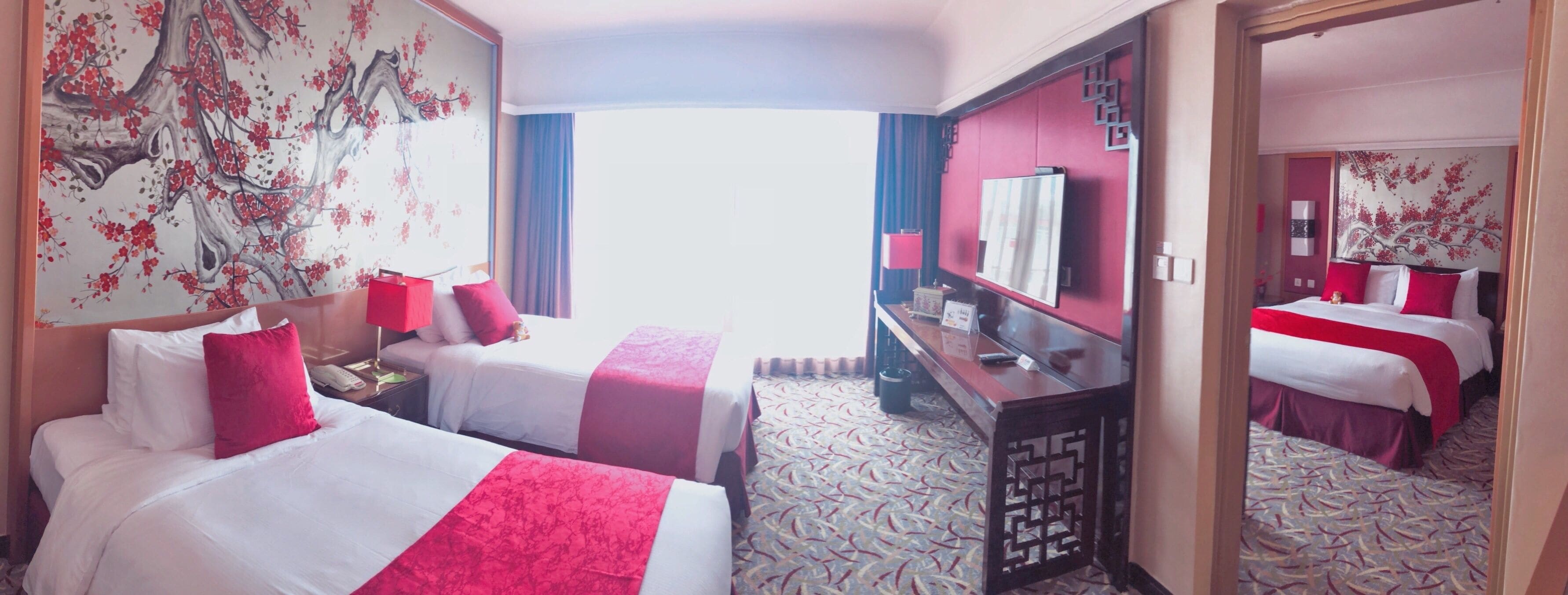 A hotel room with two beds, a desk, a television, and a large window.