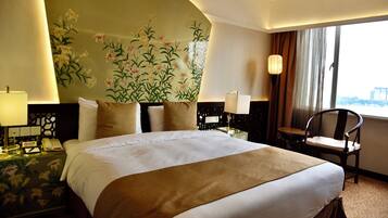 Una habitación de hotel con una cama grande, una mesita de noche con lámpara, una silla y un mural floral en la pared.