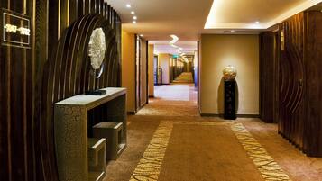 Un couloir d’hôtel, long et bordé de panneaux de bois, avec un comptoir d’accueil et une sculpture décorative.